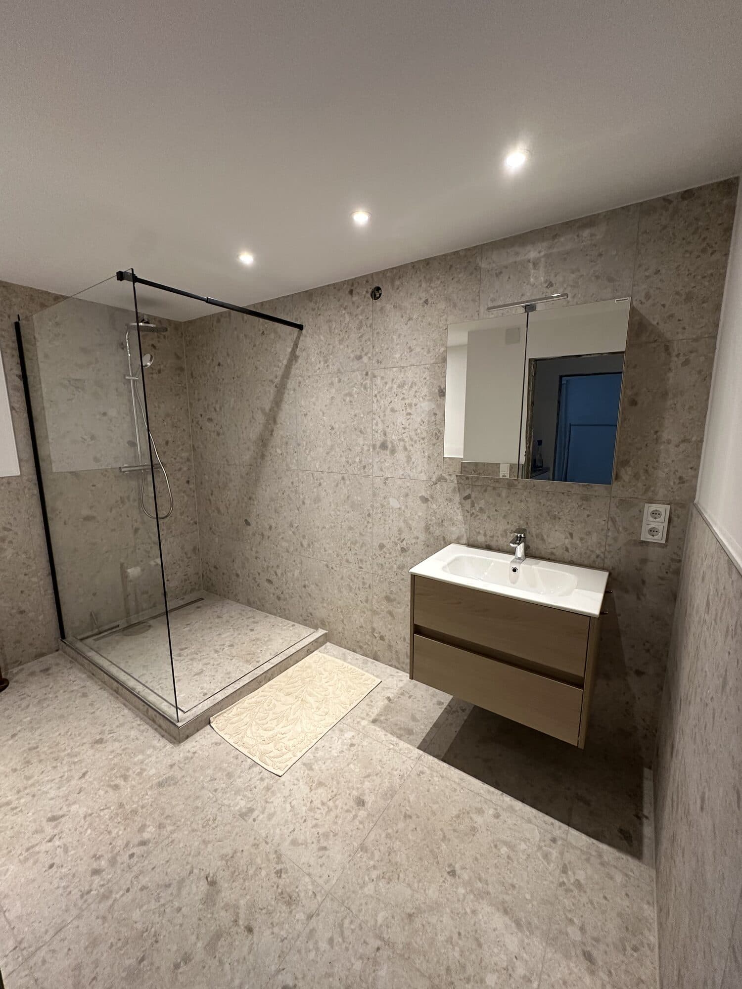 Badezimmer mit Terrazzo-Fliesen, Glasdusche und Waschtisch aus Holz