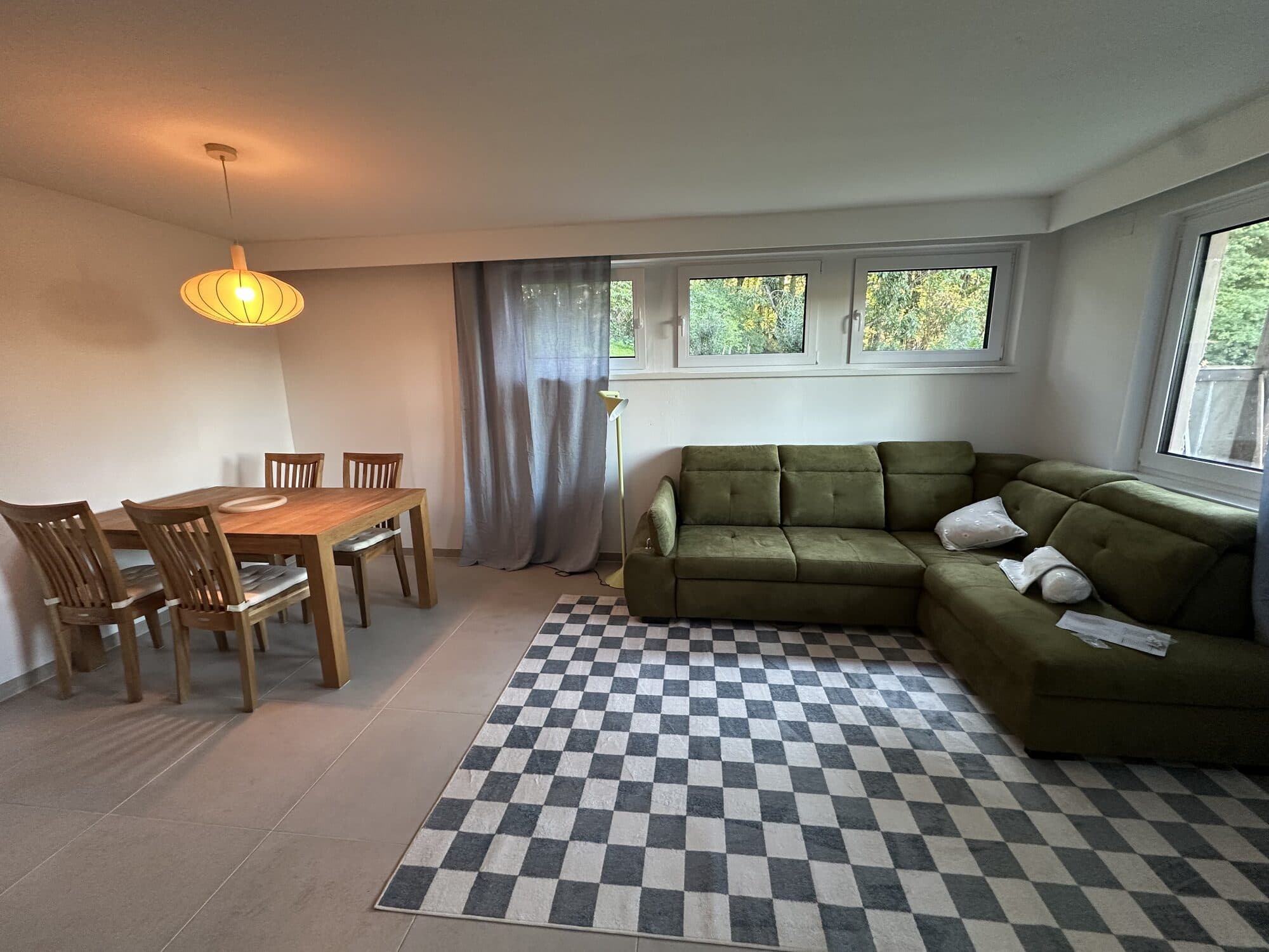 Wohnzimmer mit grünem Ecksofa, Esstisch aus Eiche und Fenstern zum Wald